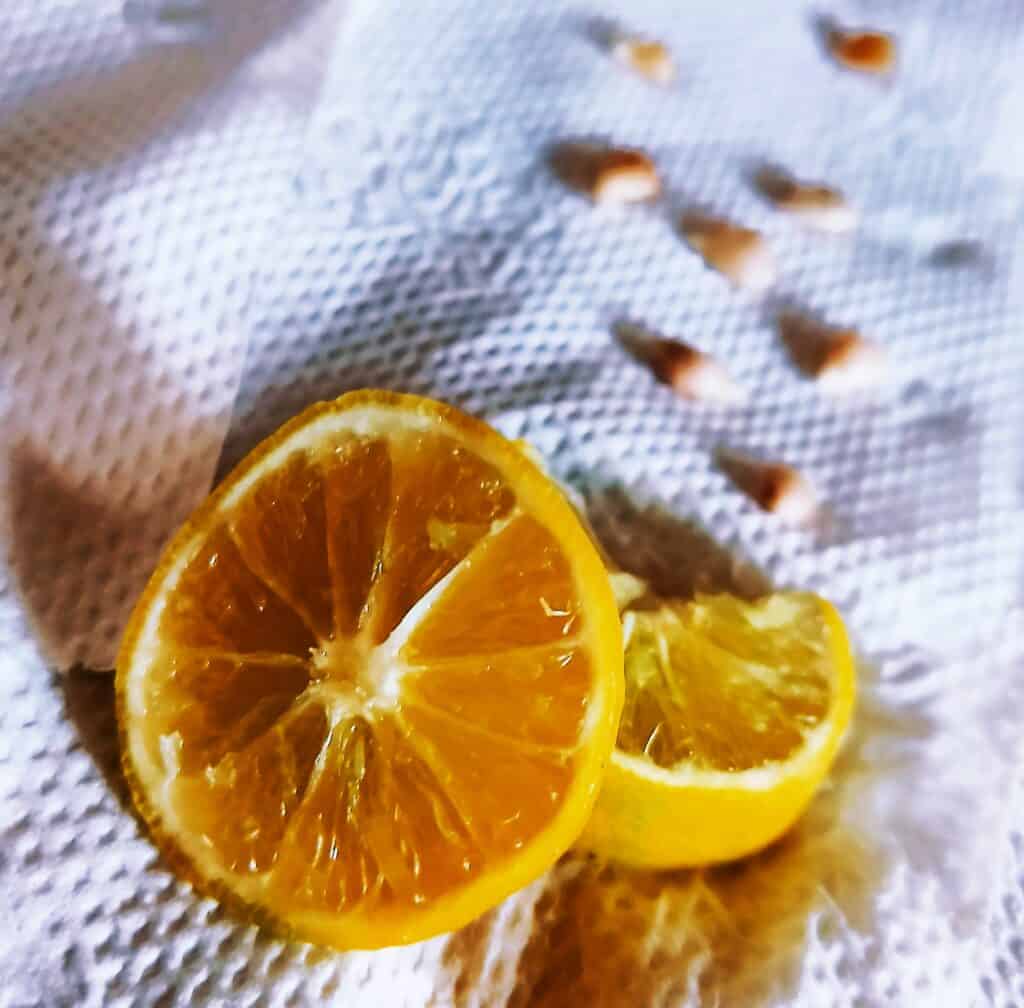 A lemon cut into half with some seeds removed on a paper towel.